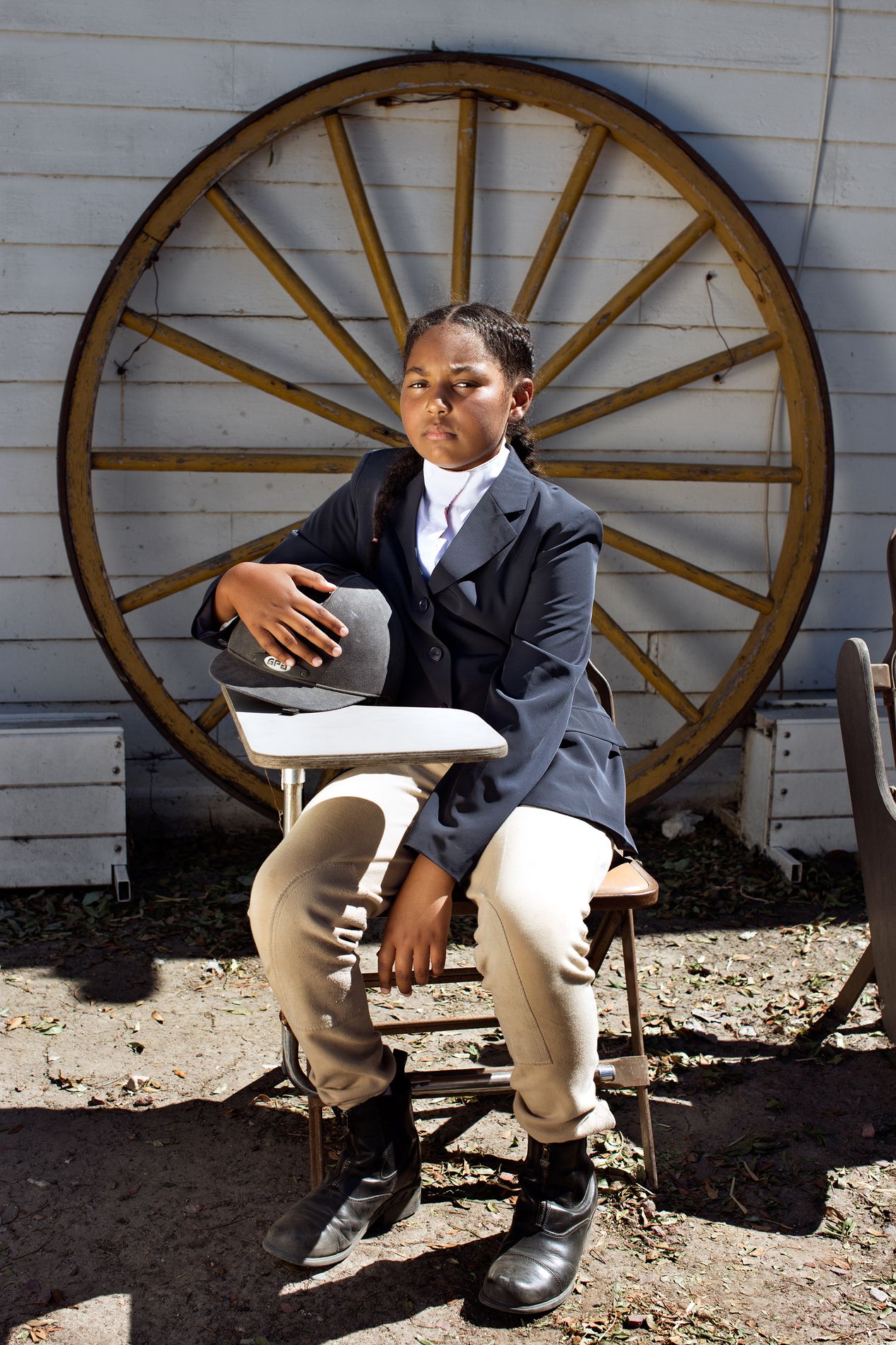 A young female equestrian sitting next to a wooden wheel.,  Ilona Szwarc, editorial photographer, Los Angeles.  
