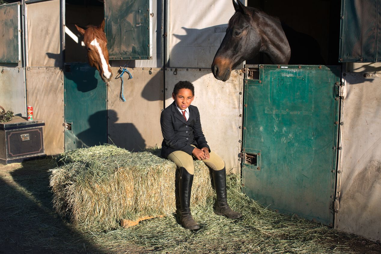 Young boy equestrian sitting in a stable, Ilona Szwarc, editorial photographer, Los Angeles. 