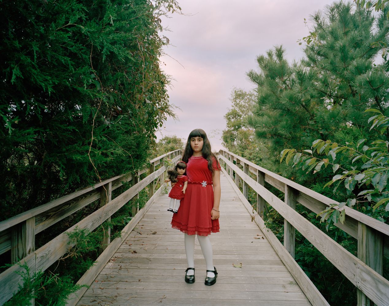 Young girl in a red dress holding a lookalike doll, environmental portrait photography, Ilona Szwarc, contemporary Los Angeles artist.