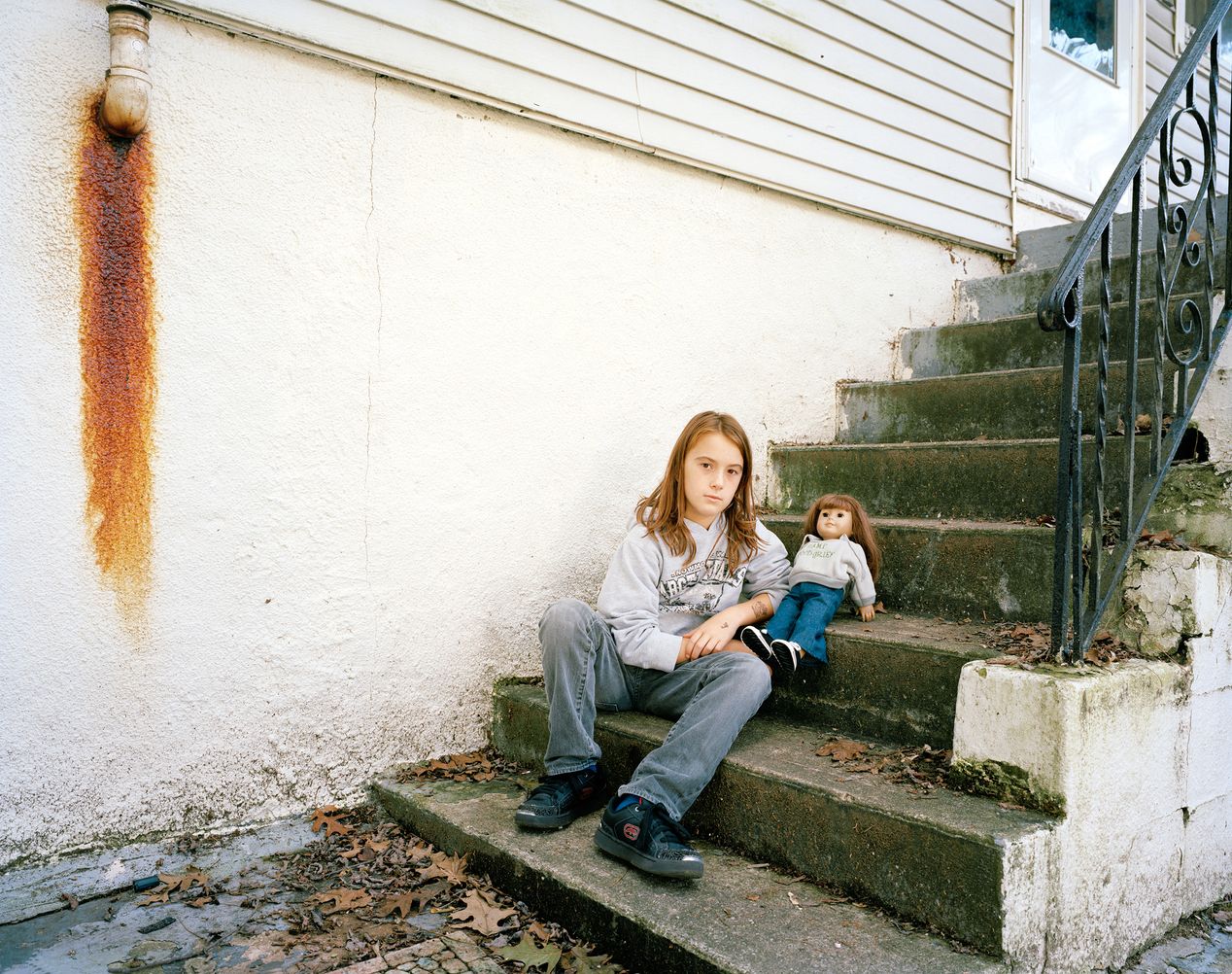 A young girl with her lookalike doll sitting on steps outside her home, environmental portrait photography, Ilona Szwarc, contemporary Los Angeles artist.