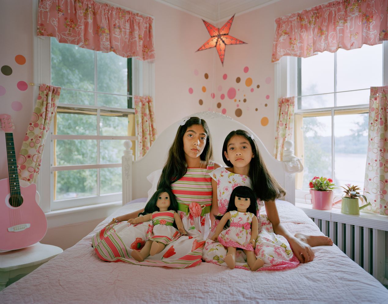 Two sisters sitting on a bed with their lookalike dolls, environmental portrait photography, Ilona Szwarc, contemporary Los Angeles artist.