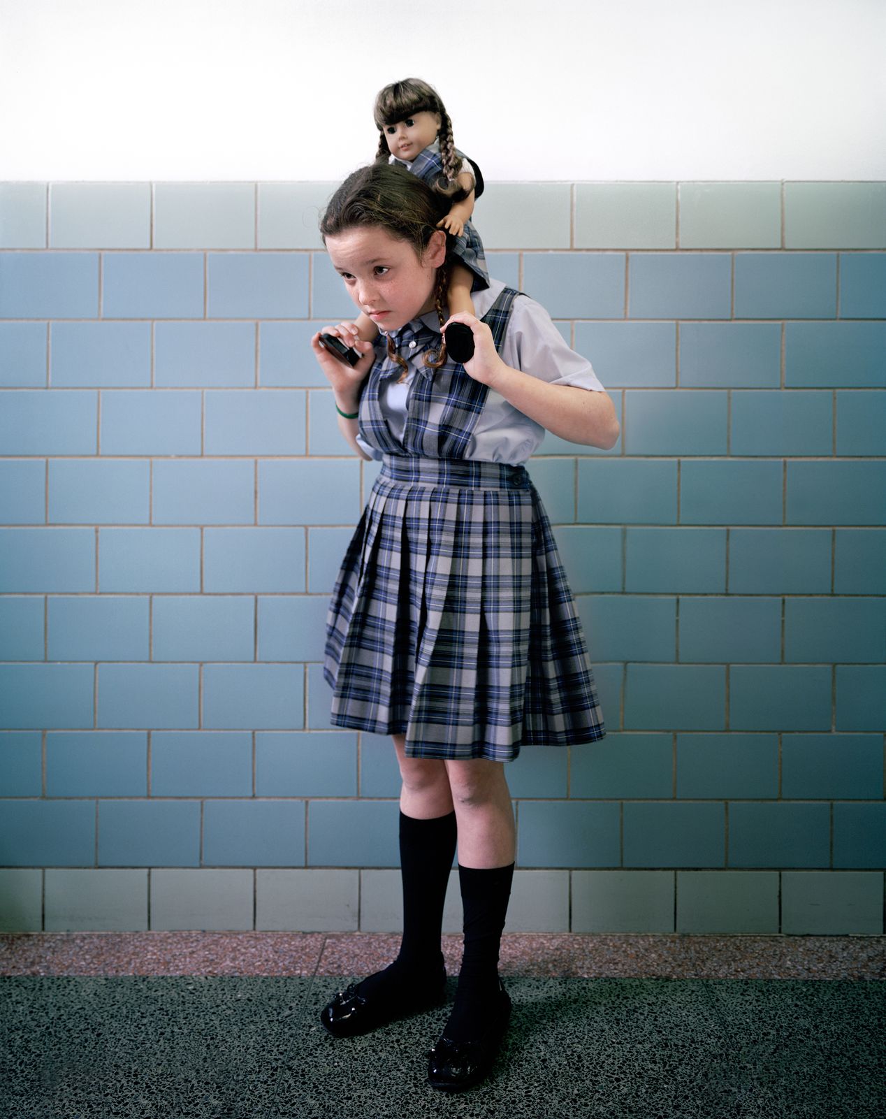 A young schoolgirl giving her lookalike doll a piggyback ride, environmental portrait photography, Ilona Szwarc, contemporary Los Angeles artist.