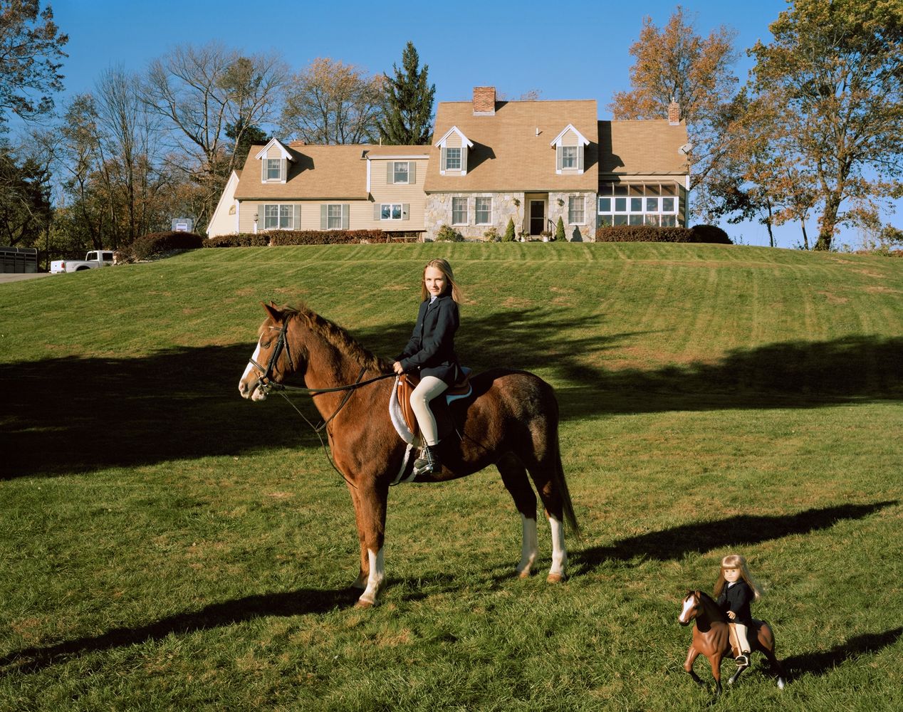 A young girl posing on her horse next to her lookalike doll on a miniature toy horse, environmental portrait photography, Ilona Szwarc, contemporary Los Angeles artist.