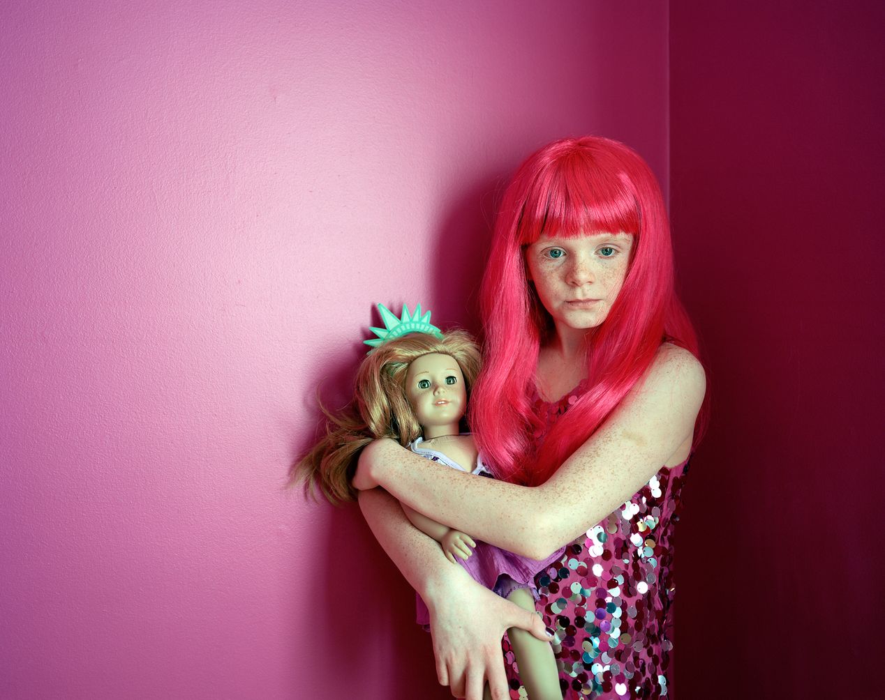 A young girl holding a doll against a bright pink wall, environmental portrait photography, Ilona Szwarc, contemporary Los Angeles artist.
