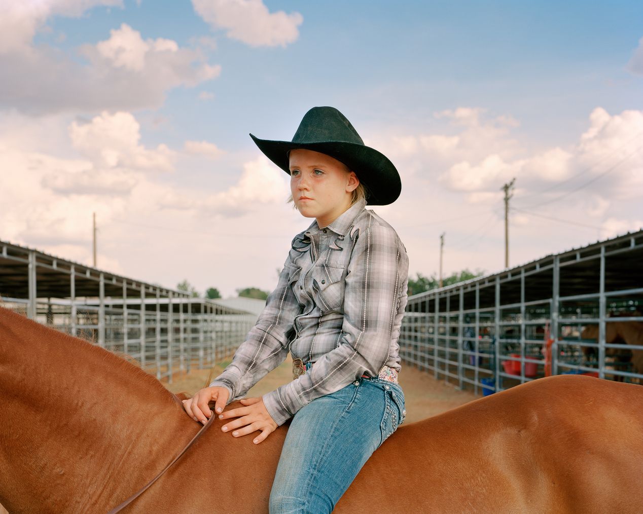 Teenage cowgirl wearing a black hat on a brown horse, environmental portrait photography, Ilona Szwarc, contemporary Los Angeles artist.