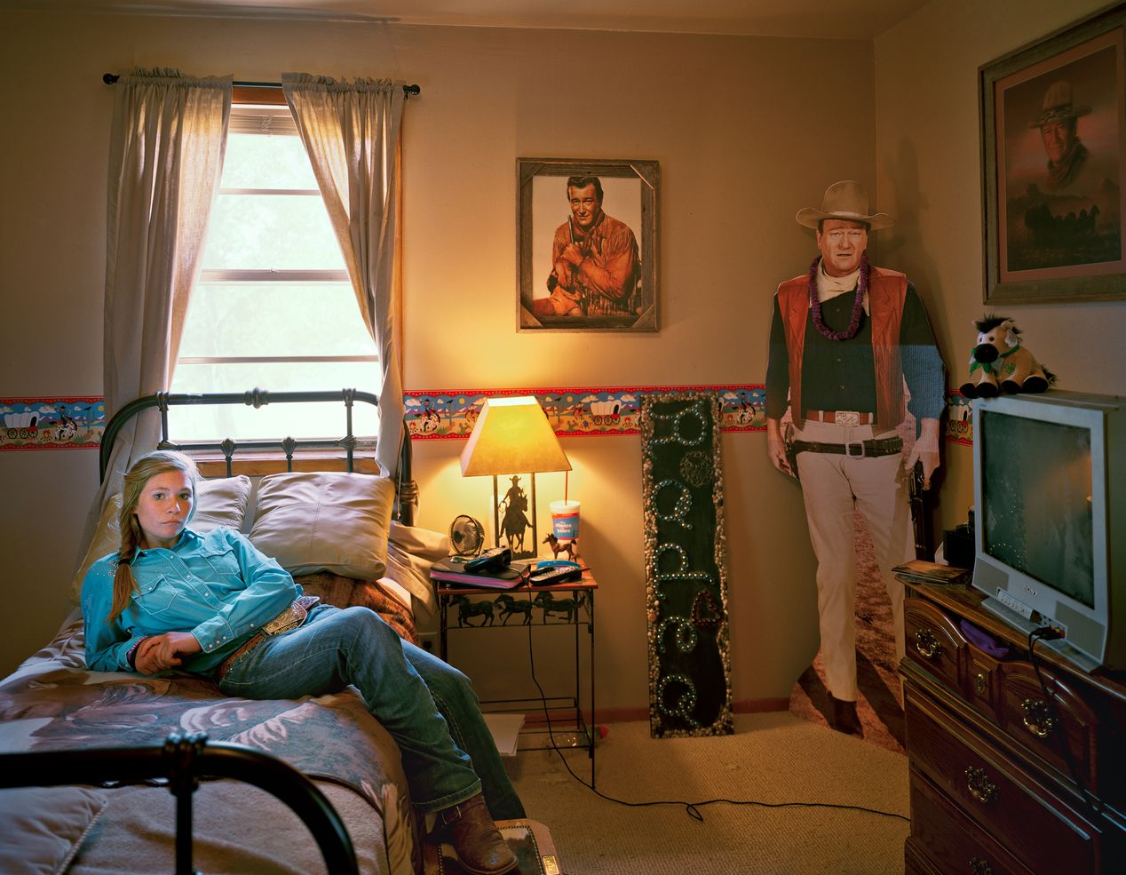 Teenage rodeo girl reclining in her John Wayne-themed room, environmental portrait photography, Ilona Szwarc, contemporary Los Angeles artist.