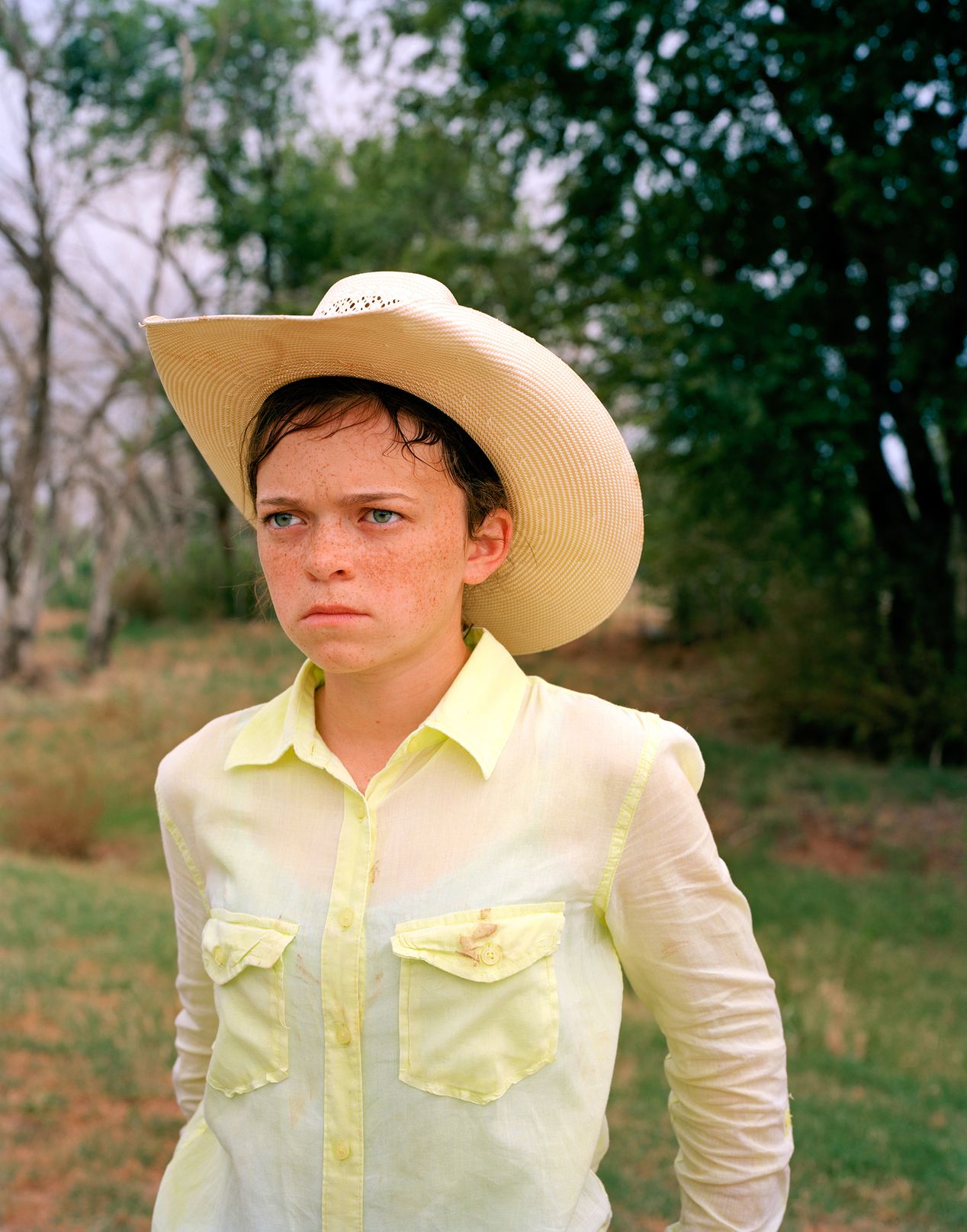 Young cowgirl in a light green shirt and a light cowboy hat, environmental portrait photography, Ilona Szwarc, contemporary Los Angeles artist.