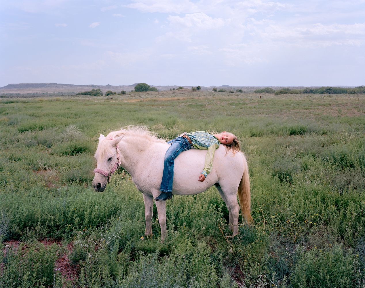 Young girl is reclining on a white pony, environmental portrait photography, Ilona Szwarc, contemporary Los Angeles artist.