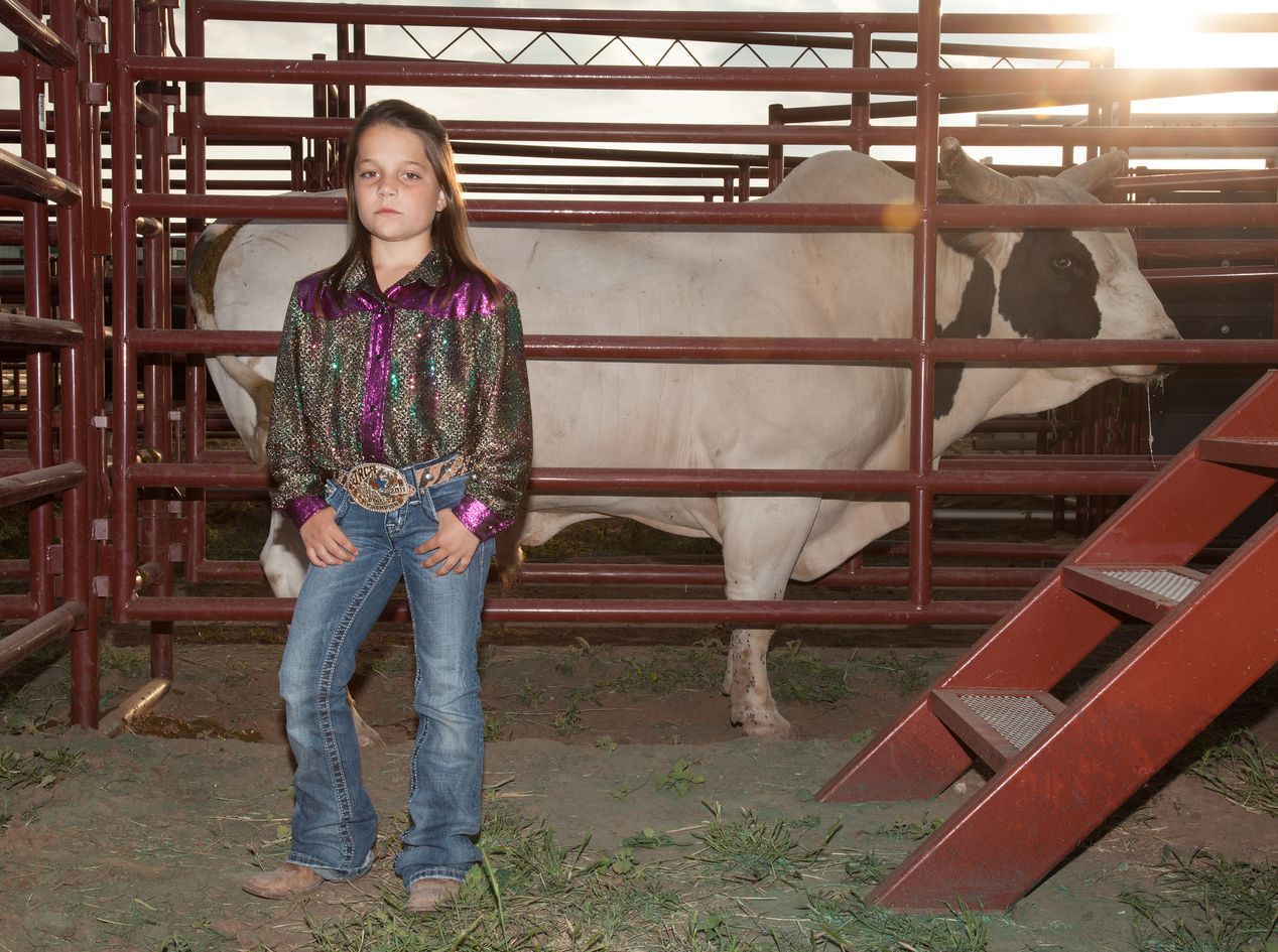 Young cowgirl standing in front of a bull stall, environmental portrait photography, Ilona Szwarc, contemporary Los Angeles artist.