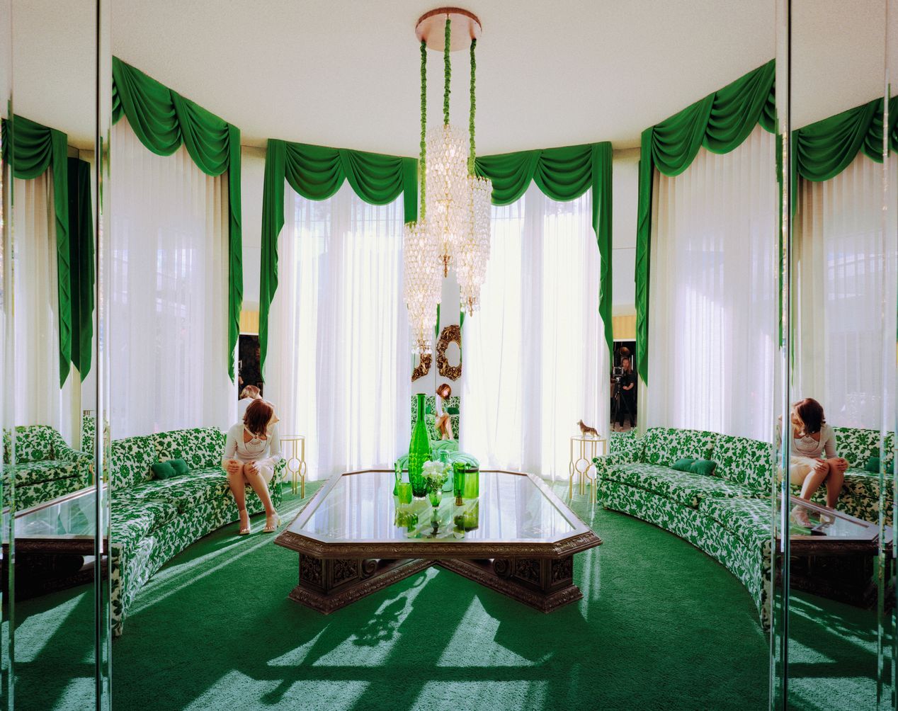 A woman, turned away is sitting in a large living room with green carpets and curtains and a green rug, art photography, Ilona Szwarc, contemporary Los Angeles artist.
