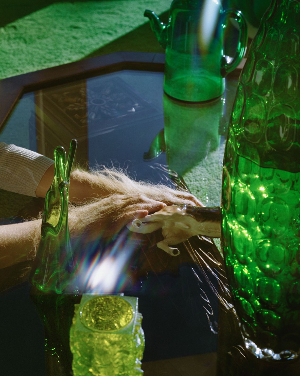 Closeup of furry hands holding onto a figurine of a dog, among green, sunlit vases, art photography, Ilona Szwarc, contemporary Los Angeles artist.